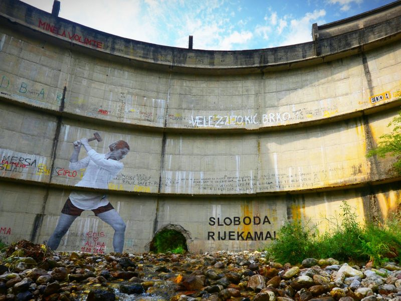 Painting a giant mural of a woman 'smashing' a broken dam on the river Baš?ica (c) Dinno Kasalo