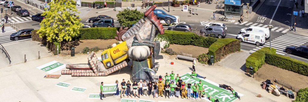 A gigantic t-rex inflatable made of fossil fuels, surrounded by activists with "Exit the Energy Charter Treay" banners