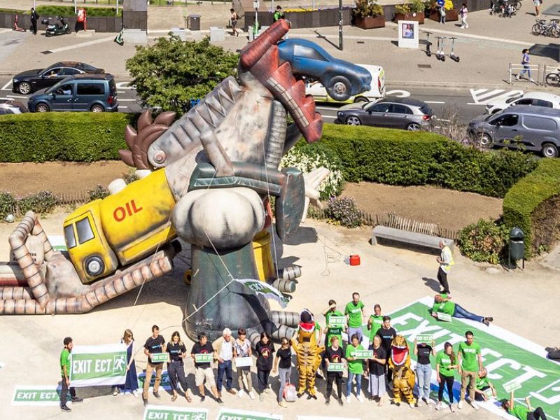 A gigantic t-rex inflatable made of fossil fuels, surrounded by activists with "Exit the Energy Charter Treay" banners