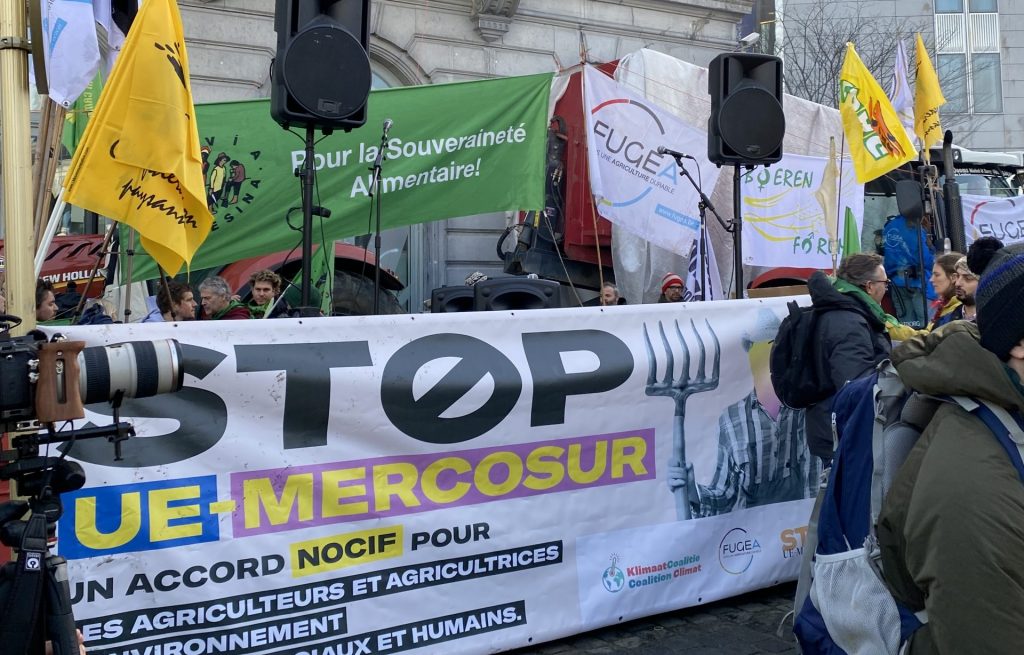 A big banner saying "Stop UE-Mercosur", surrounded by smaller flags of La Via Campesina , Confédération Paysanne, FUGEA and Boeren Forum