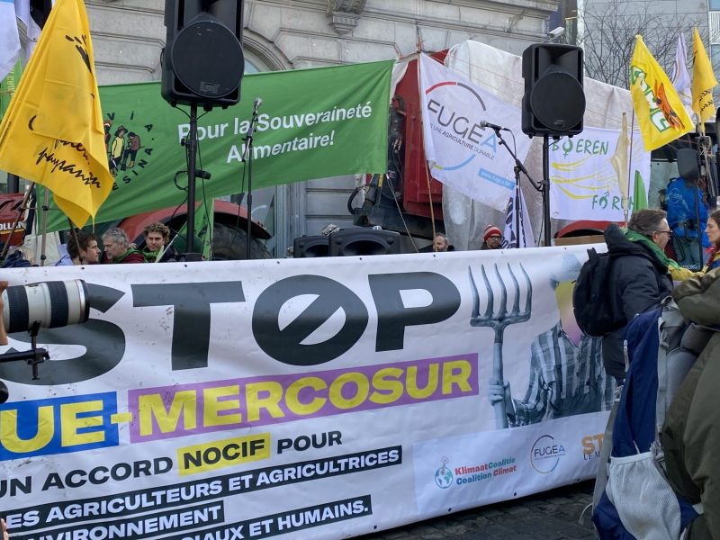A big banner saying "Stop UE-Mercosur", surrounded by smaller flags of La Via Campesina , Confédération Paysanne, FUGEA and Boeren Forum